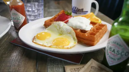 breakfast dish of two eggs and waffles with strawberries and whipped cream